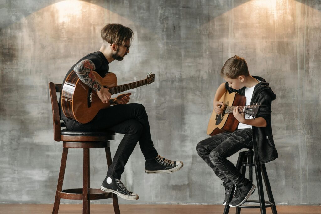 An adult man teaching a young boy to play guitar in a modern interior setting.